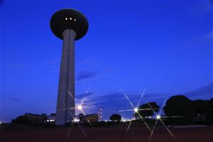 写真：夕方の空が青く染まった中、展望塔を下から撮影し、コンビナートのライトがきらめく、港公園のシンボル