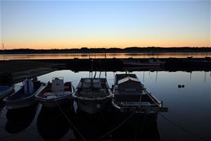 写真：晴れ渡る空に日が沈み、青からオレンジのグラデーションが一面に広がり、手前の漁船たちが影を落とす夕刻の静寂