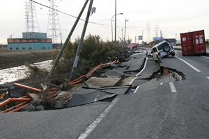 写真：川沿いの陥没した道路と落ちた車、道路の中央に着いたコンテナ