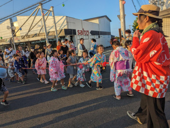写真：夏祭りで地区の子どもたちと保護者等が一緒にお神輿を引く様子。