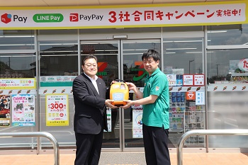 写真：成田真喜夫オーナーにバイリンガルAEDを手渡す石田市長