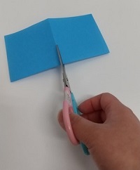 写真：半分に折った折り紙をもう一度半分に折り、はさみで切る様子