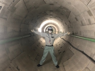 写真：巨大な排水管と手足を広げた職員