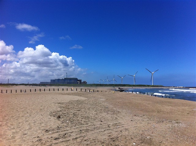 写真：青空の海岸と砂浜、並び立つ風車