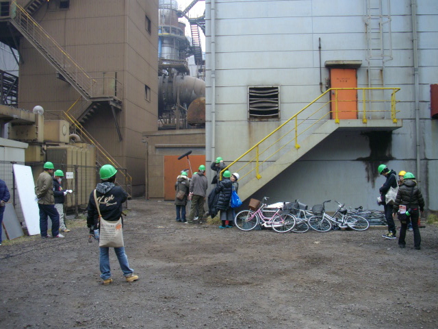 写真：工場の建物とヘルメットを着用して見学する人々
