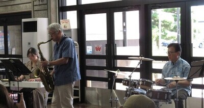 写真：8月の音楽会の風景。電子ピアノ・サックス・ドラムスで演奏する参加者