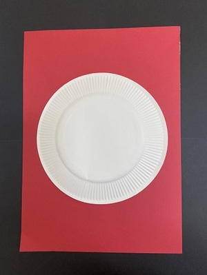 写真：赤い色画用紙の上に紙皿を置き、画用紙を円形に切り取る目安をつけているようす