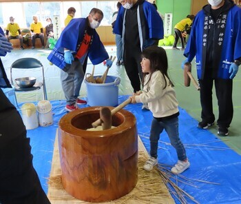 写真：幼い女の子が餅つきしているのを見守る大人たち