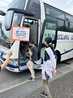 写真：かみす子育てウェルカムバスツアーの旗を掲げている大型バスに参加者親子が笑顔で乗車する様子