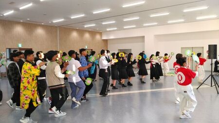 写真：手に団扇をもち参加者全員で笑顔を浮かべながら踊る講師と参加者