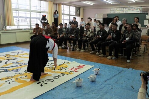 写真：書道パフォーマンスを披露する波崎高校の生徒。それを熱心に見届ける技能実習生達