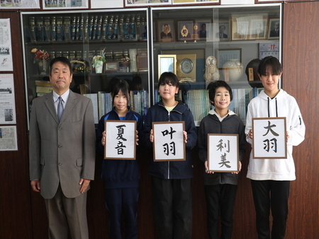 写真：軽野小学校にて撮影。「夏音」「叶羽」「利美」「大羽」という文字が書かれたパネルを持つ子どもたちと学校の先生