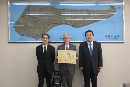写真:2025年4月8日撮影。感謝状を掲げる訪問者を間に挟んで立つ行政センター所長と市長