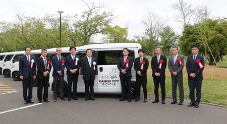 写真：2025年4月22日撮影。電気自動車の前で出席者9人と市長で記念撮影