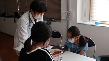 写真:医師の指導の下、参加者が二人一組になり血圧測定を体験するようす