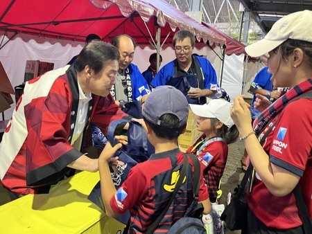 写真:2025年9月13日メルカリスタジアムにて撮影。特産品を市民へ手渡す市長