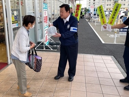 写真:2025年10月10日撮影。スーパーに買い物をしに来た市民へ、市長が啓発品を手渡しているようす