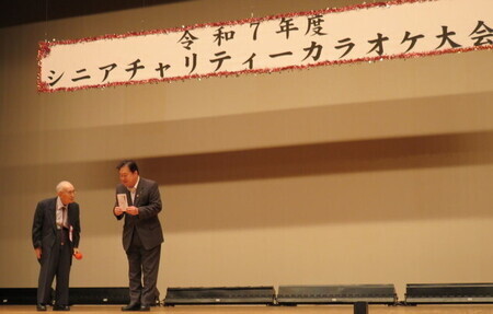 写真：2025年10月19日撮影。カラオケ大会の壇上で寄付金を受け取る市長