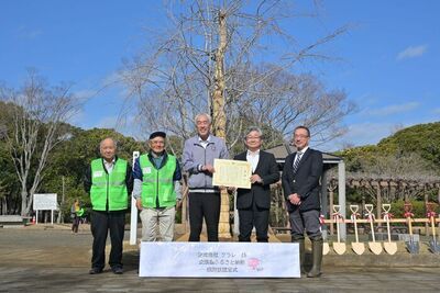 写真：2026年3月7日撮影。植樹した桜の前で記念撮影する市長と訪問者4名。