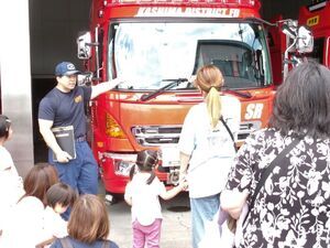写真：消防署の職員から消防車の説明を聞いている親子
