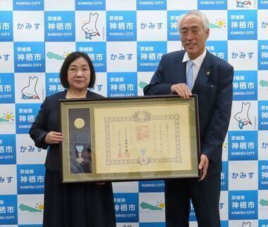 写真：表彰状と勲章を入れた額縁を手に受賞者と並んで記念撮影する市長
