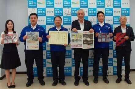 写真：寄贈された読売KODOMO新聞を両手に持ち、みなと運送株式会社のみなさんと並んで写真を撮影する市長